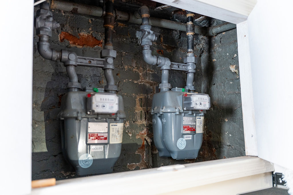 Two residential gas meters mounted inside a utility enclosure with black steel gas piping